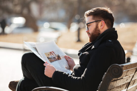 Man in glasses sitting and reading newspaper at the city